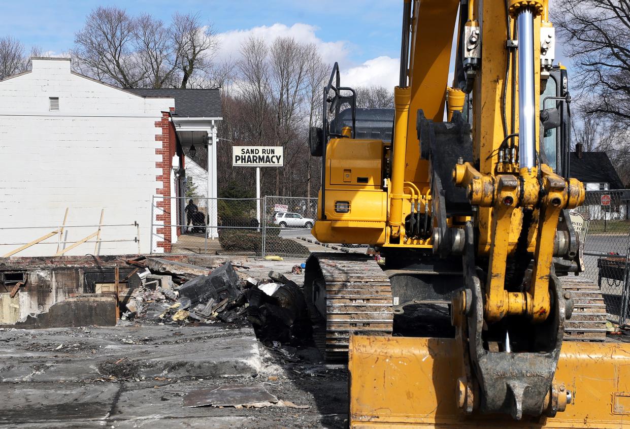 An Akron resident is framed by wreckage and heavy equipment as they walk into Sand Run Pharmacy on Feb. 20.