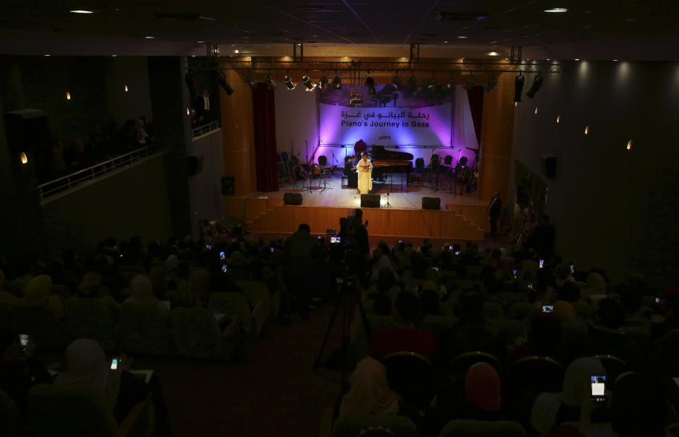 Japanese pianist Kaoru Imahigashi plays the piano while opera singer Fujiko Hirai, right, perform as the audience films by their mobiles during a concert to mark the debut of Gaza's only grand piano after it was rescued from conflict, at a theater nestled in the Palestinian Red Crescent Society's building in Gaza City, Sunday, Nov. 25, 2018. The only grand piano in the Gaza Strip is debuting to the public for the first time in over a decade after its restoration. (AP Photo/Adel Hana)