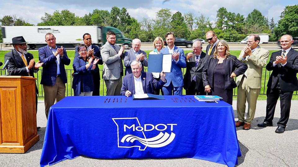 Gov. Mike Parson, seated, holds aloft a ceremonial copy of House Bill 4 on Tuesday surrounded by Missouri lawmakers, Columbia Mayor Barbara Buffaloe and other representatives in the Parkade Center Parking lot that faces Interstate 70. Lawmakers approved a $2.8 billion expansion of I-70 in May. It was just awaiting Parson's signature.