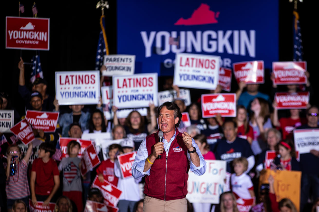 Glenn Youngkin at the microphone surrounded by supporters carrying banners bearing his name and saying Latinos for Youngkin.