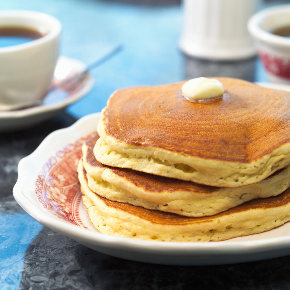 A stack of three pancakes with a pat of butter on top on a patterned plate, with a cup of coffee in the background. Image categorized as Internet Finds