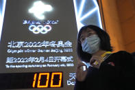A supporter makes a gesture with her hands near a countdown clock as it crosses into the 100 days countdown to the opening of the Winter Olympics in Beijing, China, Tuesday, Oct. 26, 2021. (AP Photo/Ng Han Guan)
