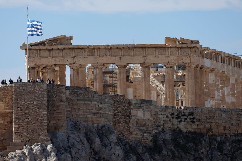 Greek flag flutters in front of the Parthenon Temple atop the Acropolis in Athens