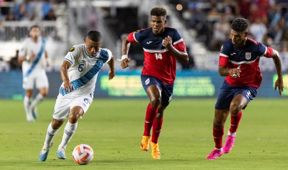 El jugador de Guatemala Carlos Mejía (izq.) trata de pasar la marca de los cubanos Neisser Sandó (der.) y Modesto Méndez, en el partido de la Copa Oro celebrado el 27 de junio de 2023 en el DRV PNK Stadium de Fort Lauderdale, Florida.