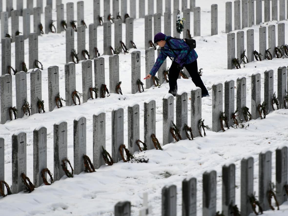 A person places a poppy after laying wreaths on headstones with Wreaths Across Canada at the National Military Cemetery of Canada in Ottawa, on Sunday, Dec. 5, 2021. (Justin Tang/Canadian Press - image credit)