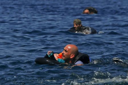 A Syrian refugee holding a baby in a life tube swims towards the shore after their dinghy deflated some 100m away before reaching the Greek island of Lesbos, September 13, 2015. REUTERS/Alkis Konstantinidis