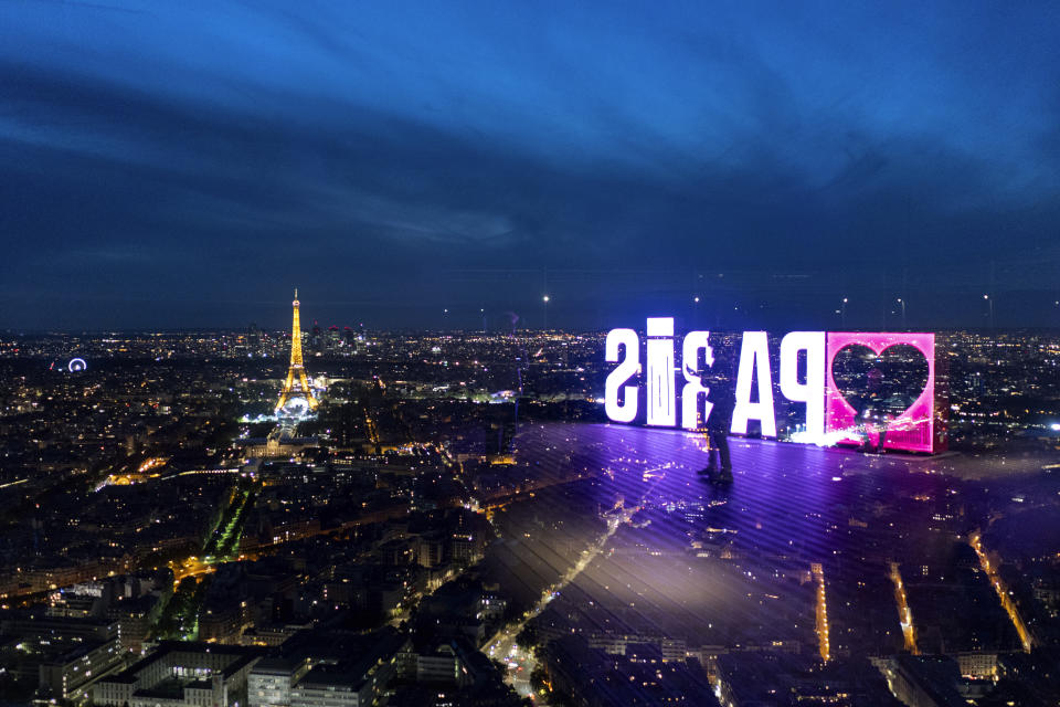 Un visitante camina por el cartel de "París" reflejado en el muro de vidrio en la zona de observación de la torre de Montparnasse, previo a los Juegos Olímpicos de París, el martes 23 de julio de 2024. (AP Foto/David Goldman)