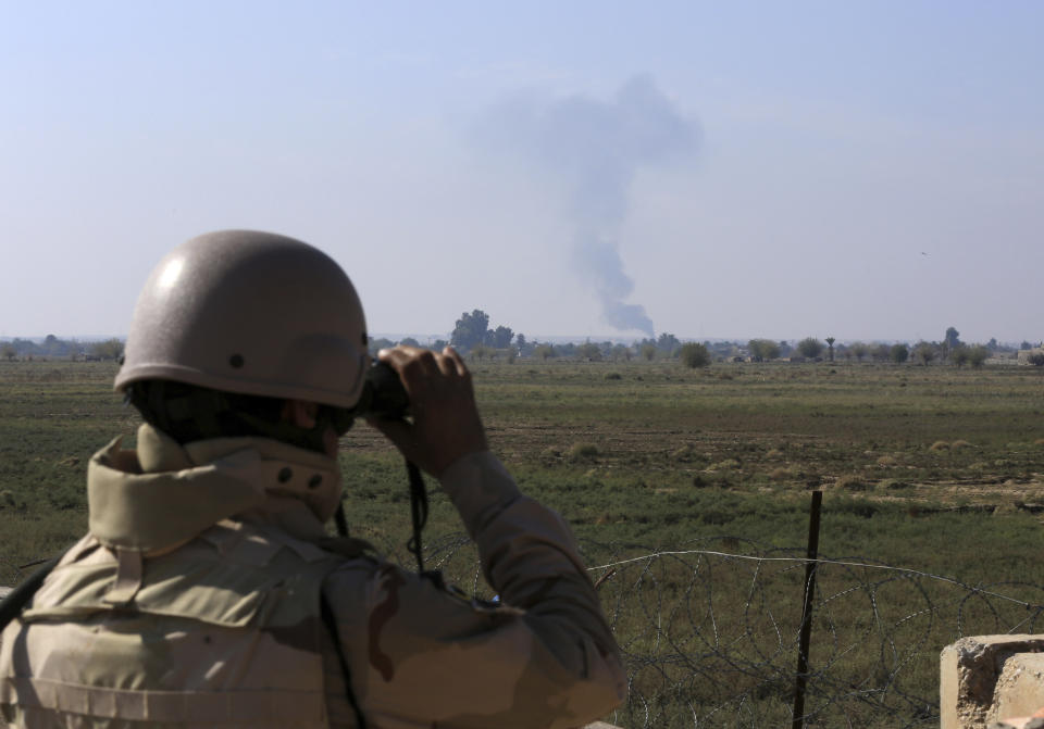 In this Tuesday, Nov. 13, 2018 photo, an Iraqi soldier watches smoke rising after an airstrike by US-led International coalition warplanes against ISIS, on the border between Syria and Iraq in Qaim, Anbar province, Iraq. More than a year after this Iraqi town was freed from the Islamic State group, booms from airstrikes still echo and columns of smoke are visible, rising beyond the earthen berms and concrete walls marking the border with Syria. On the other side, the fight is raging to capture one of the militant group’s last enclaves. (AP Photo/Hadi Mizban)
