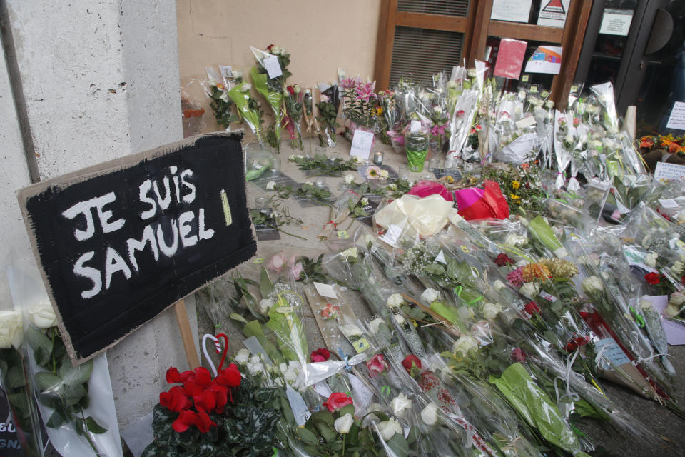 FILE - In this Oct.17, 2020 file photo, a poster reading "I am Samuel" and flowers lay outside the school where slain history teacher Samuel Paty was working, in Conflans-Sainte-Honorine, northwest of Paris. French lawmakers tackle a bill on Monday to dig up radical Islam by its roots in the country, beliefs that authorities maintain are creeping into public services, associations, some schools and online with the goal of undermining national values. (AP Photo/Michel Euler, File)