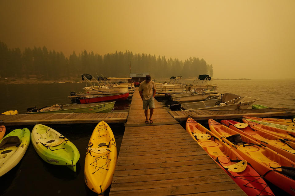 A business owner, who declined to give his name, walks next to kayaks he rents as smoke from the Creek Fire fills the sky, Sunday, Sept. 6, 2020, in Shaver Lake, Calif. (AP Photo/Marcio Jose Sanchez)