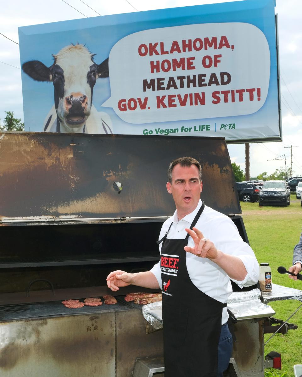 Gov. Kevin Stitt loads up a grill with beef on May 12, 2021, under a billboard that PETA has along SE 15 Street in Oklahoma City.