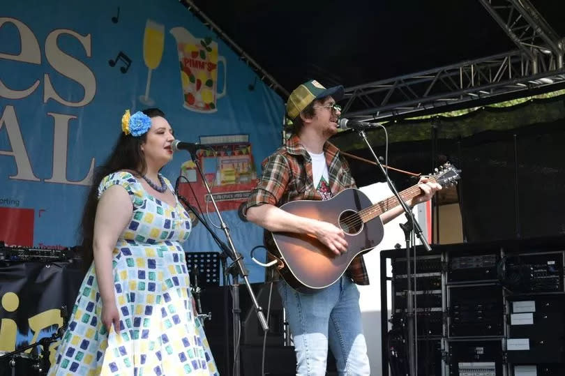 Two  performers singing, one with a guitar, on the main stage