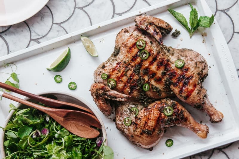 Grilled spatchcocked chicken on a platter with a bowl of salad