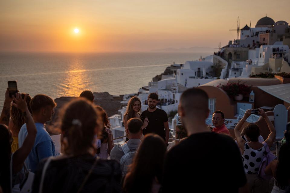 A couple poses for a photo as tourists line up to take a photo as they view Santorini’s famed sunset, at Santorini, Greece,