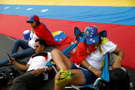 Opposition supporters sit next to a giant Venezuelan national flag as they block a highway, during a protest against Venezuelan President Nicolas Maduro's government in Caracas, Venezuela May 15, 2017. REUTERS/Carlos Garcia Rawlins