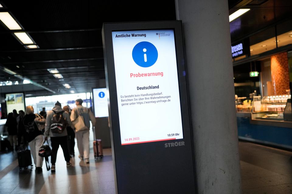 People pass screens displaying a nation wide test alarm message at the main train station in Berlin, Germany, Thursday, Sept. 14, 2023. Warning messages were blaring on cell phones, public displays and deafening alarms sounded across Germany in a nationwide test alert. The screen reads: "Official Warning- Test Alarm Germany There is no need for action Report your observations at https://warntag-umfrage.de."