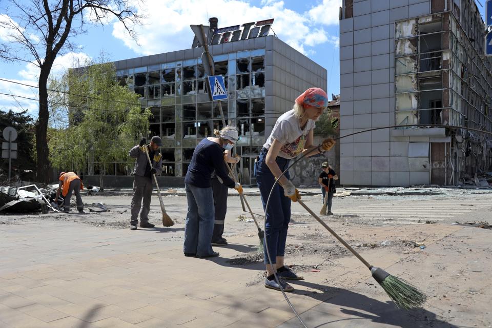Volunteers clean a street next to damaged buildings in Mariupol, in territory under the government of the Donetsk People's Republic, eastern Ukraine, Wednesday, April 27, 2022. Municipal services and volunteers began clearing rubble and cleaning the city. (AP Photo/Alexei Alexandrov)