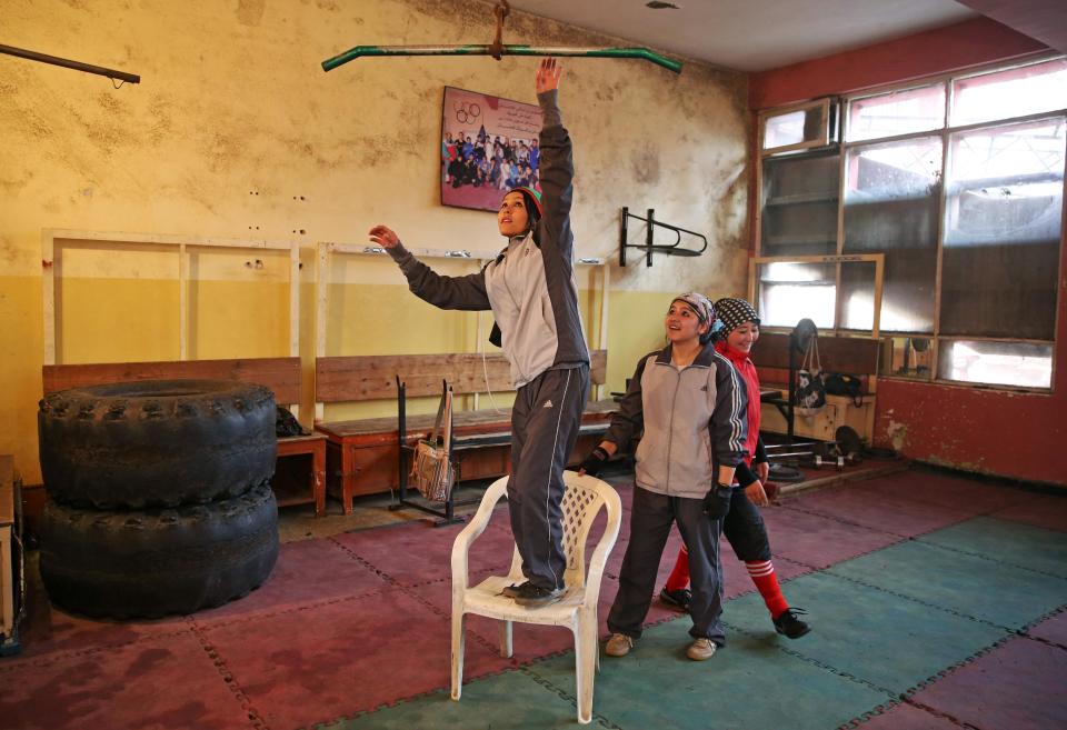 In this Wednesday, March, 5, 2014 photo, an Afghan female boxer, left, tries to do pull-ups during a practice session at the Kabul Stadium boxing club, Afghanistan. The Afghanistan National Olympic Committee boxing club has fewer than a dozen women and little money for them. Previously nongovernmental organizations supported them. At that time there were 25 young women who received a salary the equivalent of $100 per month and transportation to and from the Kabul Stadium where they train. (AP Photo/Massoud Hossaini)