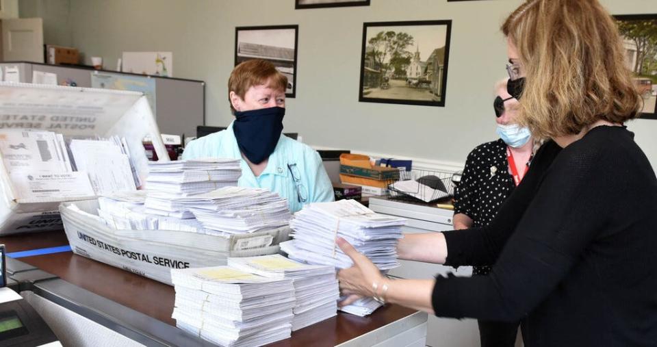 Barnstable Town Clerk Ann Quirk looks on as Janet Murphy, right, brings in another pile from the morning mail in July 2020 to add to a growing stack of applications for mail-in ballots for voting for the 2020 primary and presidential elections in her office at Barnstable Town Hall. Barnstable County voters in particular, as Cape towns have had some of the state's highest rates of mail-in voting in recent elections.