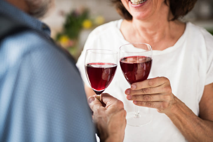 A senior couple in clinking glasses with red wine is pictured.