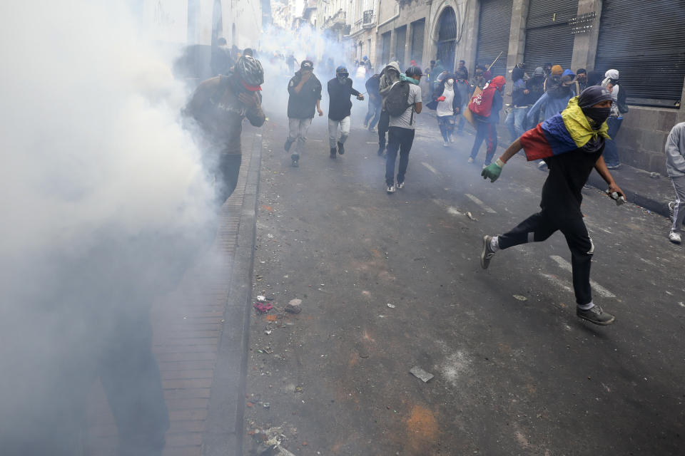 Protesters take cover from tear gas launched by police during clashes in downtown Quito, Ecuador, Wednesday, Oct. 9, 2019. Ecuador's military has warned people who plan to participate in a national strike over fuel price hikes to avoid acts of violence. The military says it will enforce the law during the planned strike Wednesday, following days of unrest that led President Lenín Moreno to move government operations from Quito to the port of Guayaquil. (AP Photo/Fernando Vergara)