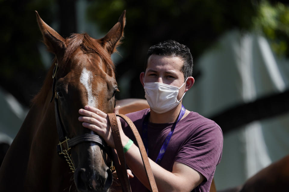 In this Friday, May 22, 2020 photo, a groom wearing a face mask leads a horse to the track at Santa Anita Park in Arcadia, Calif. Horse racing returned to the track after being idled for one and a half months because of public health officials' concerns about the coronavirus pandemic. (AP Photo/Ashley Landis)