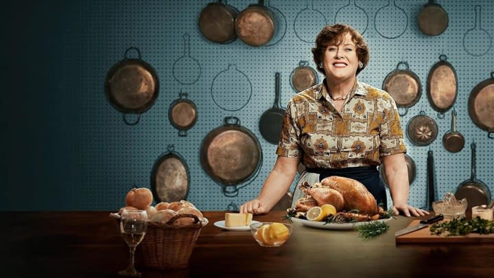 Julia Child standing behind a table filled with bread in a scene from Julia.