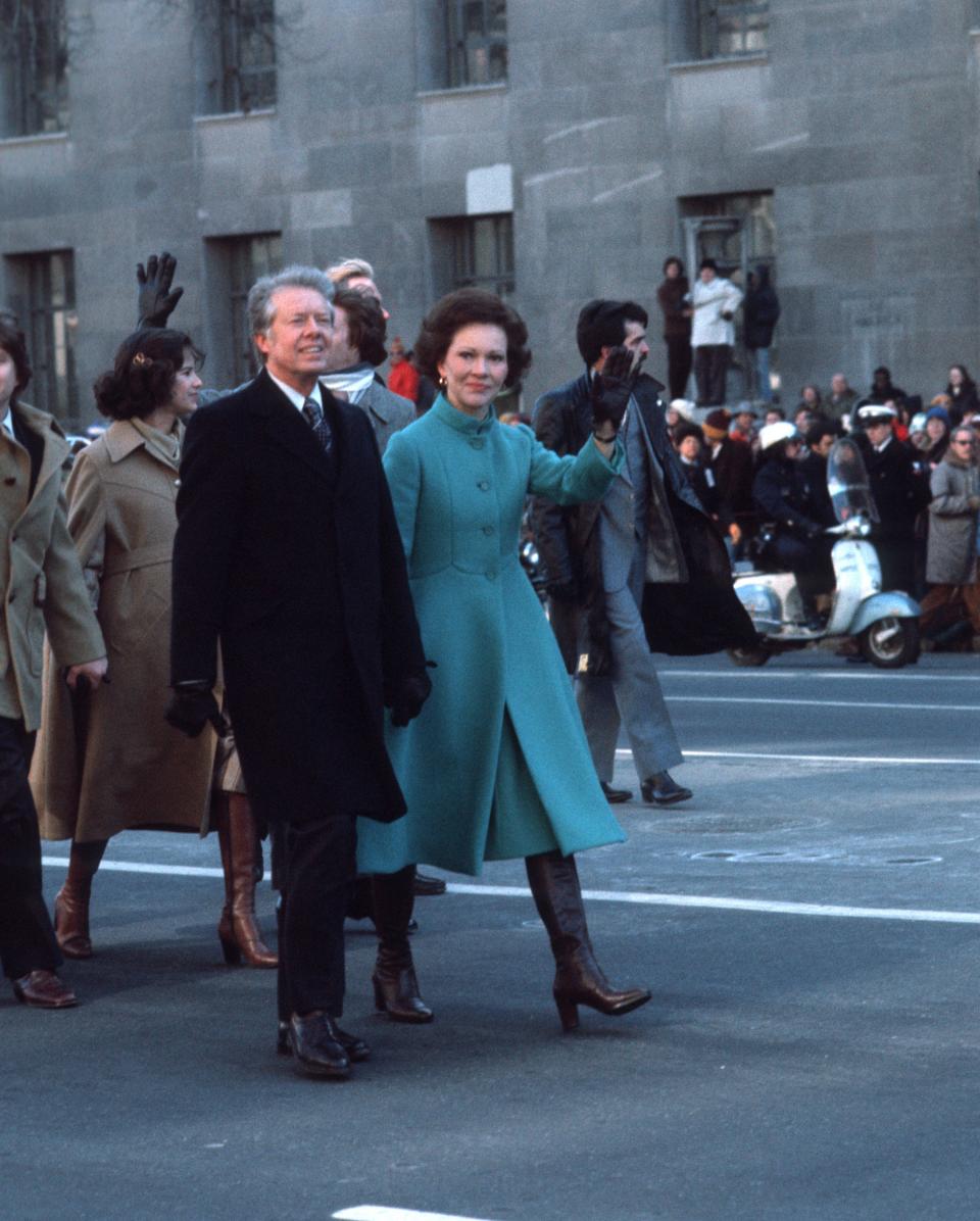 Jimmy Carter walking with Rosalynn Carter in a turquoise knee-length coat and black nee-high boots.