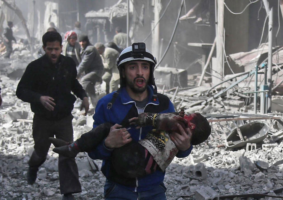 <p>A Syrian civil defence member carries an injured child rescued from between the rubble of buildings following government bombing in the rebel-held town of Hamouria, in the besieged eastern Ghouta region on the outskirts of the capital Damascus, on Feb. 19, 2018. (Photo: Abdulmonam Eassa /AFP/Getty Images) </p>