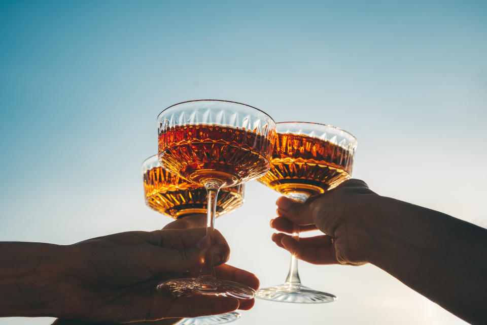 A close-up shot of friends clinking sparkling wine glasses at sunset