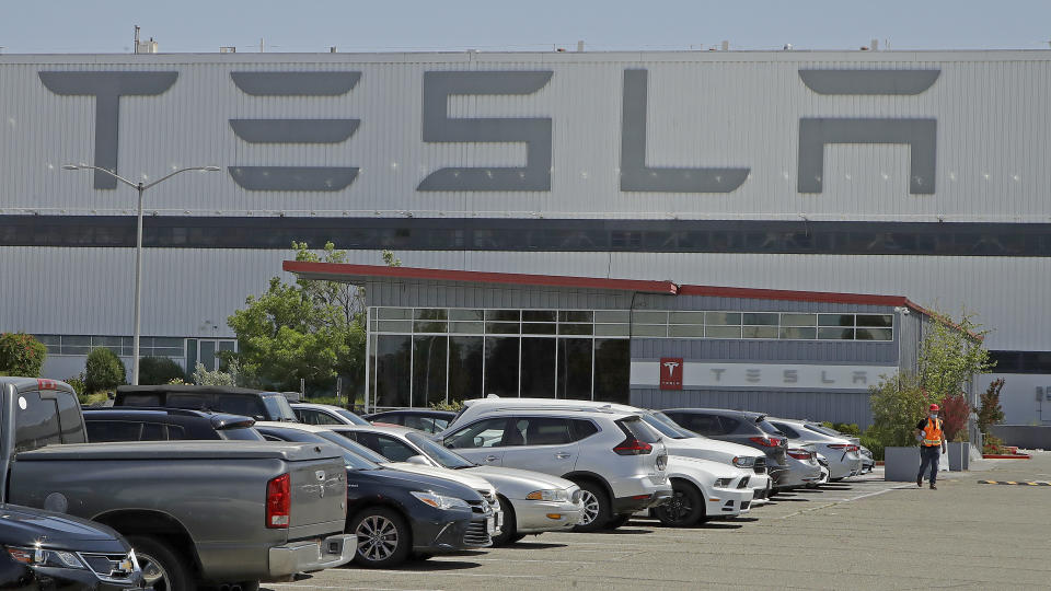 FILE - In this May 11, 2020, file photo, a man walks in the Tesla plant parking lot in Fremont, Calif. Tesla says it delivered more electric vehicles worldwide in the second quarter than it did in the first. The increase came even though coronavirus restrictions forced it to shut down its only U.S. factory for much of the period. (AP Photo/Ben Margot, File)