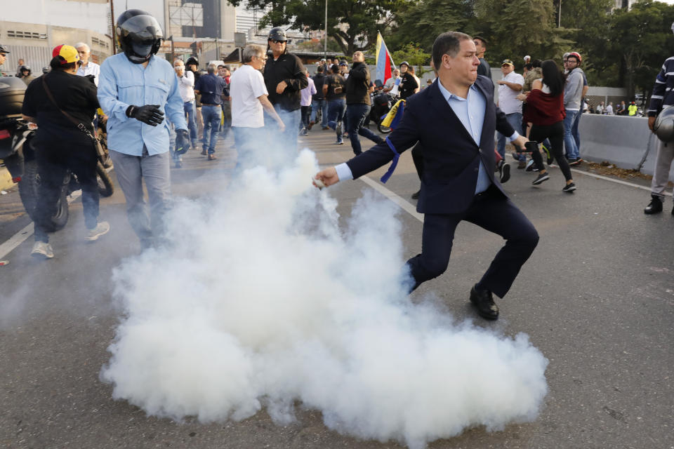 Un opositor al presidente venezolano Nicolás Maduro devuelve una lata de gas lacrimógeno lanzada por personal militar que vigila la base aérea de La Carlota en Caracas, el lunes 29 de abril de 2019. (AP Foto/Ariana Cubillos)