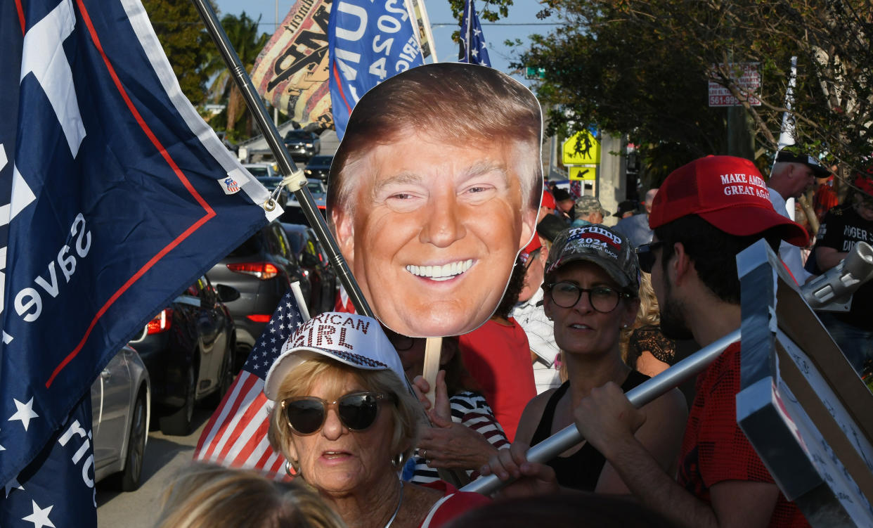 Supporters of Donald Trump wave signs and flags as they wait for the former president's motorcade.