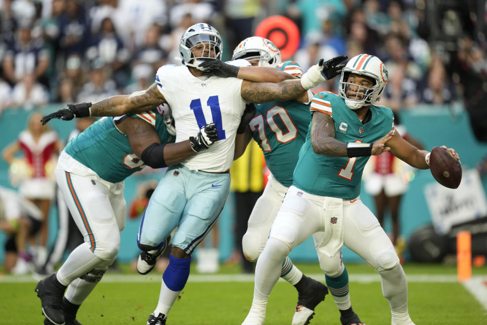 Miami Dolphins quarterback Tua Tagovailoa (1) stands back to pass as Dallas Cowboys linebacker Micah Parsons (11) is held back by offensive tackle Kendall Lamm (70) during the first half of an NFL football game, Sunday, Dec. 24, 2023, in Miami Gardens, Fla. (AP Photo/Rebecca Blackwell)