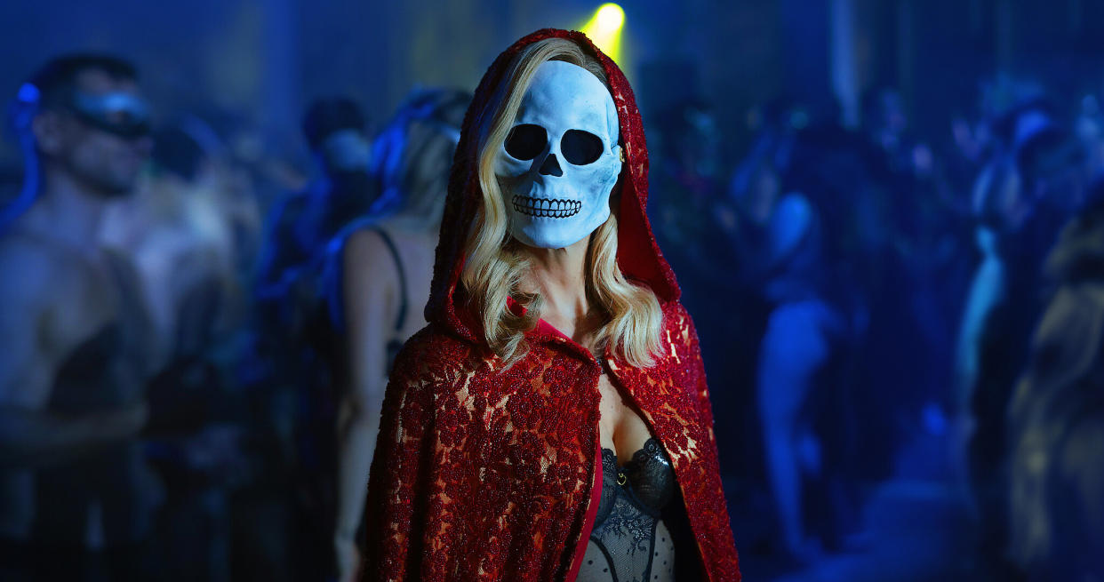  A woman wearing a red cloak and skull mask. 