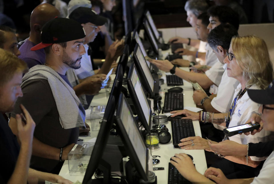 FILE - In this July 14, 2018, file photo, people, left, talk to tellers while placing bets at the Meadowlands Racetrack, in East Rutherford, N.J. Dozens of states are rushing to capitalize on the U.S. Supreme Court lifting a federal ban on sports gambling. (AP Photo/Julio Cortez, File)