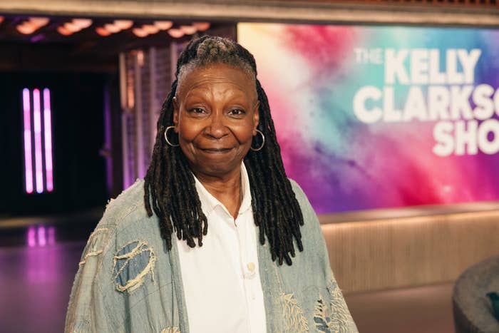 Whoopi Goldberg smiling, wearing a denim jacket, on The Kelly Clarkson Show set