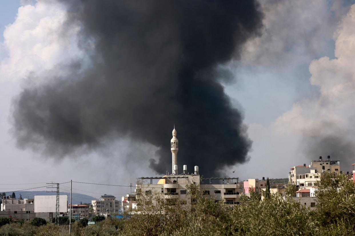 Plumes of smoke rise beyond a tower.