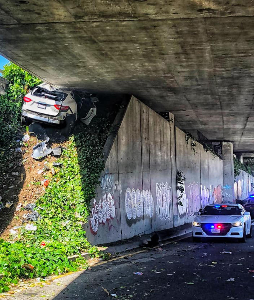 In this photo provided by the California Highway Patrol is the scene where a man fleeing from the CHP totaled his girlfriend's Maserati SUV after he careened up an embankment and slammed into the underside of an overpass, wedging the car under a freeway in Oakland, Calif., on Monday, April 12, 2021. (California Highway Patrol via AP)