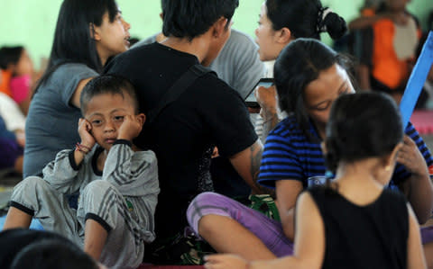 A boy sits behind his parents and villagers after being evacuated - Credit: SONNY TUMBELAKA/AFP/Getty Images