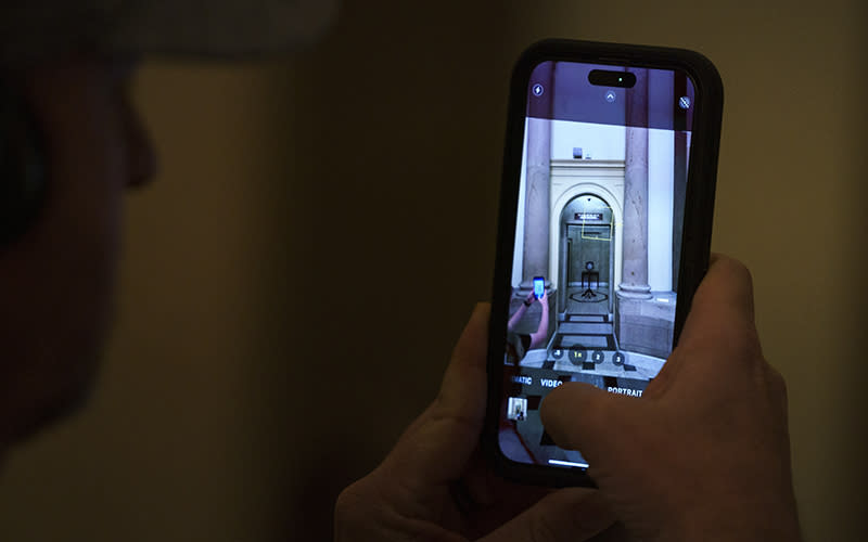 A closeup is shown of a person's phone. The person holding the phone is using the camera to take a photo of former Speaker McCarthy's (R-Calif.) office.