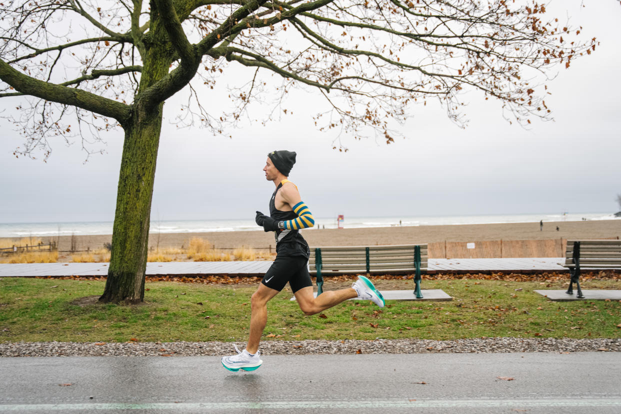 man running in black shorts, white running shoes and black tank top near beach in winter, best men's running shoes in 2024, I run competitively — here are the best men's running shoes in 2024 for marathons, casual runs and competitions (photo via Alex Cyr).