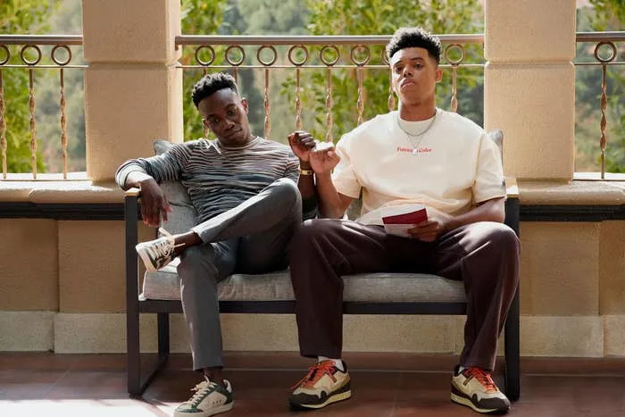 Olly Sholotan and Jabari Banks sit on a bench outside, dapping it up in a scene from the show