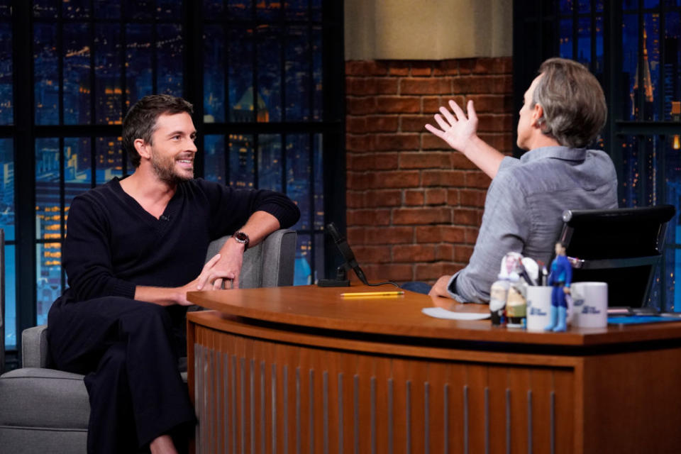 Jonathan Bailey sits in an interview with Seth Meyers on a talk show set, engaging in conversation