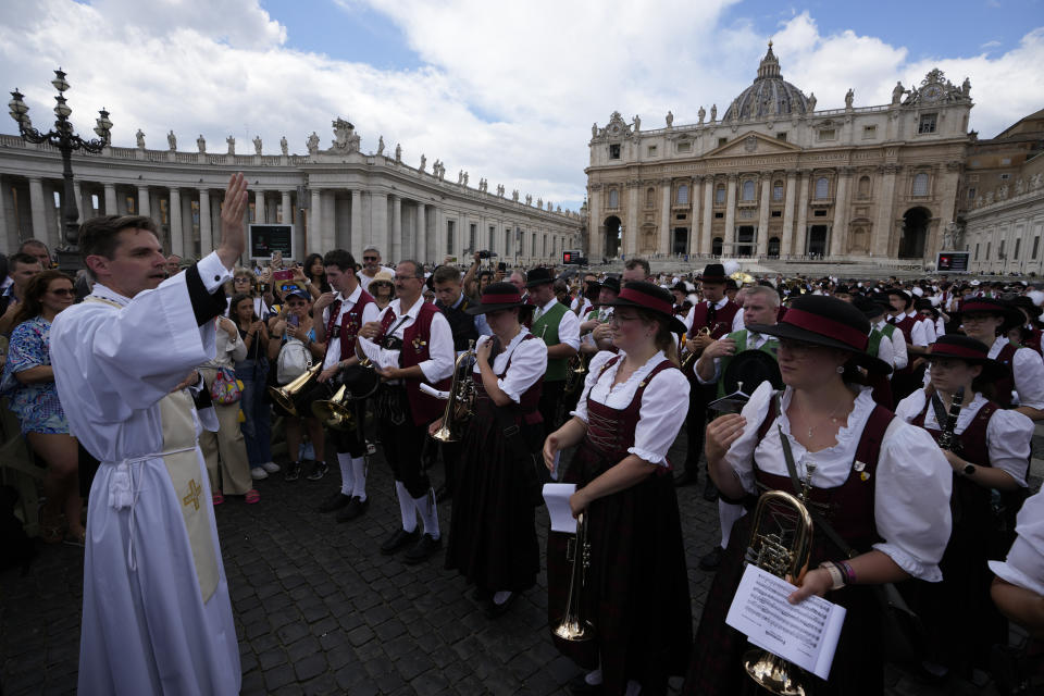 A priest blesses the members of a German folk band in front of the Apostolic Palace at The Vatican from where popes bless faithful on Sunday's noon,Sunday, June 11, 2023. Pope Francis, following doctors' advice, skipped Sunday's customary public blessing to allow him to better heal after abdominal surgery. (AP Photo/Alessandra Tarantino)