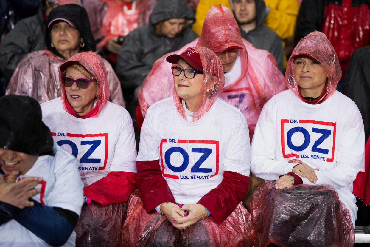 Three women with OZ T-shirts and red plastic head coverings wait for Trump to speak.