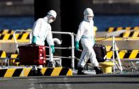 Officers in protective gears carry luggage cases after people who were transferred from cruise ship Diamond Princess, arrive at a maritime police's base in Yokohama