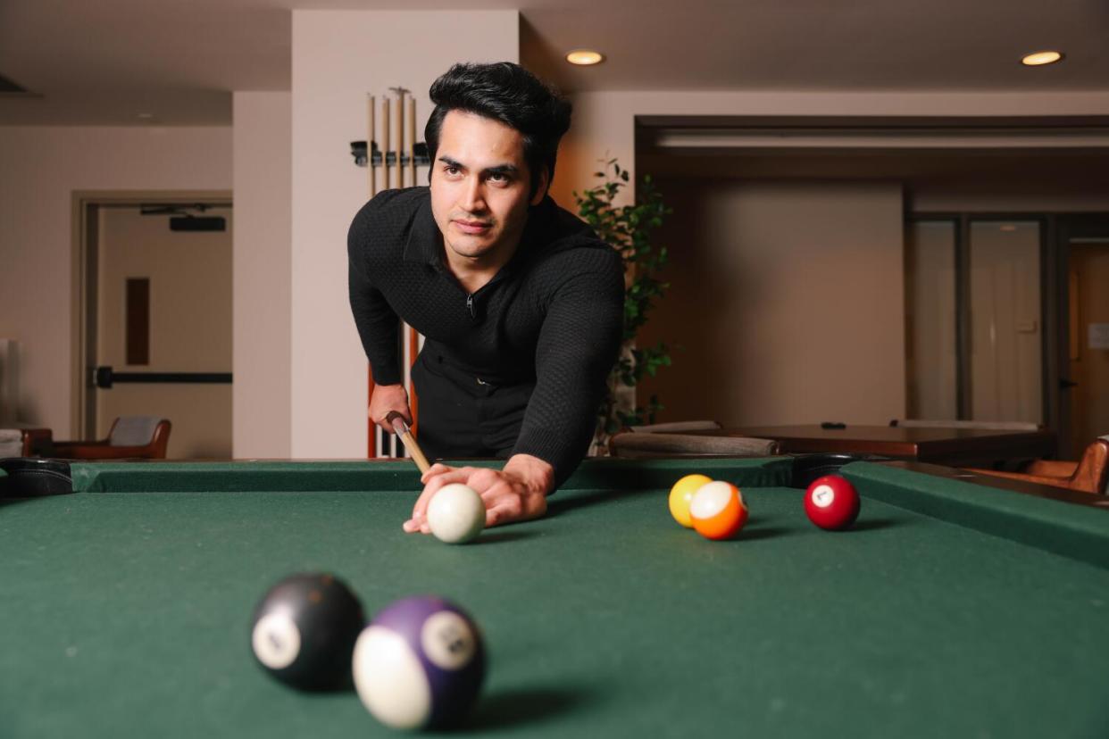 A man in a black shirt playing billiards at a green felt pool table.