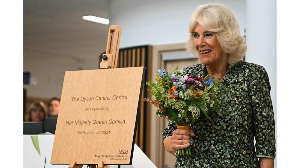 camilla holding bouquet of flowers next to wooden plaque