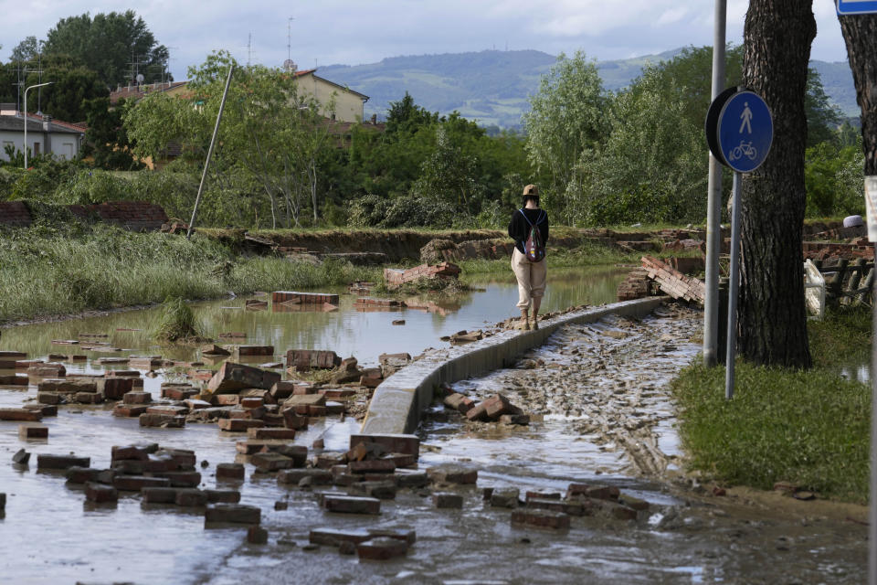 Claudia, a Faenza resident, walks past the a road flooded by Lamone river in Faenza, Italy, Thursday, May 18, 2023. Exceptional rains Wednesday in a drought-struck region of northern Italy swelled rivers over their banks, killing at least eight people, forcing the evacuation of thousands and prompting officials to warn that Italy needs a national plan to combat climate change-induced flooding. (AP Photo/Luca Bruno)